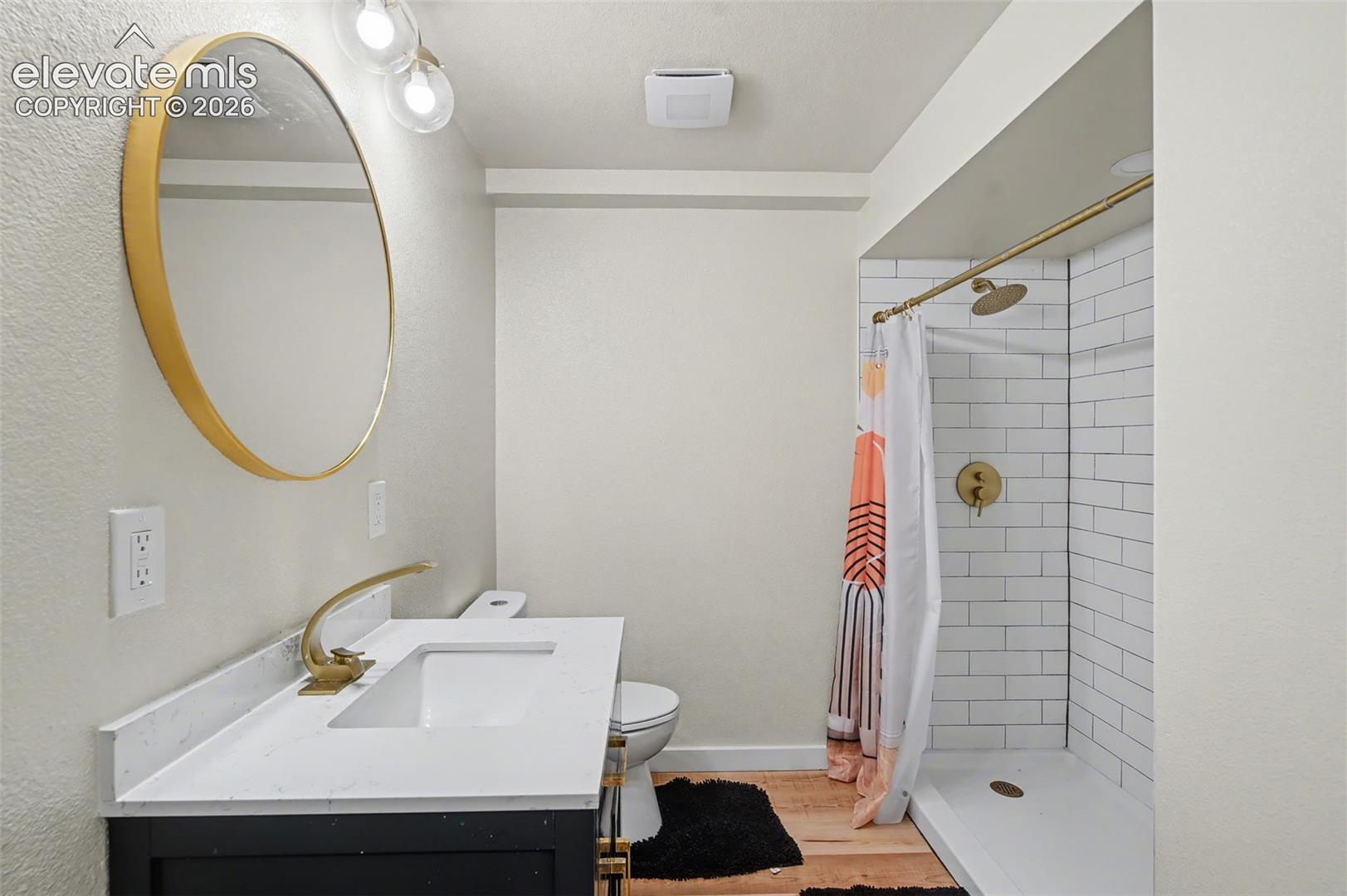 Bathroom featuring a dark-finish vanity with a white countertop and integrated sink, round brass-framed mirror, brass faucet, and a shower with white subway tile surround and brass hardware