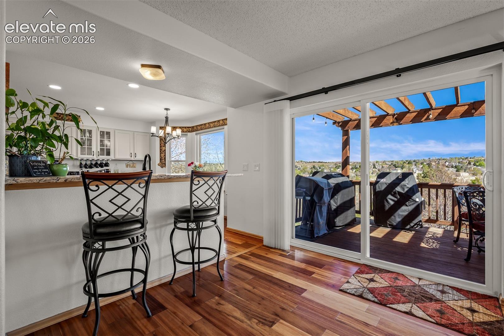 Wide sliding glass doors open to the upper outdoor deck with a pergola and seanic view.