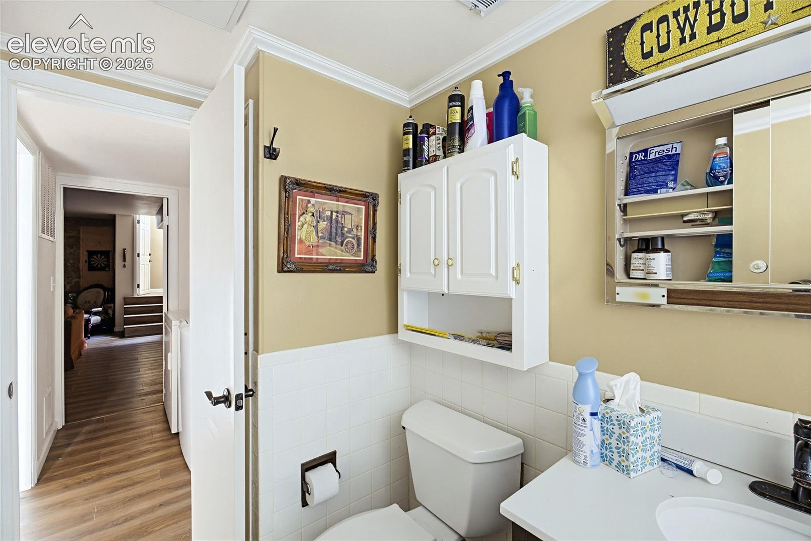 Bathroom featuring white wall tile wainscoting, white built-in wall cabinetry, a mirrored medicine cabinet with integrated lighting, and wood-finish flooring