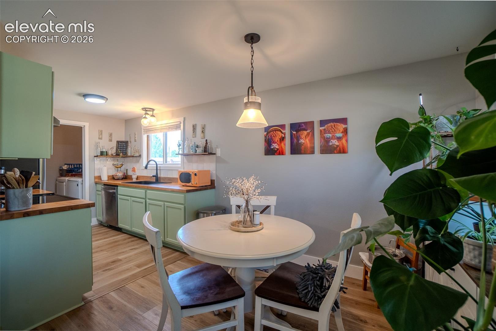 Open-concept kitchen featuring light green cabinetry with wood countertops, stainless steel dishwasher, and wood-finish flooring