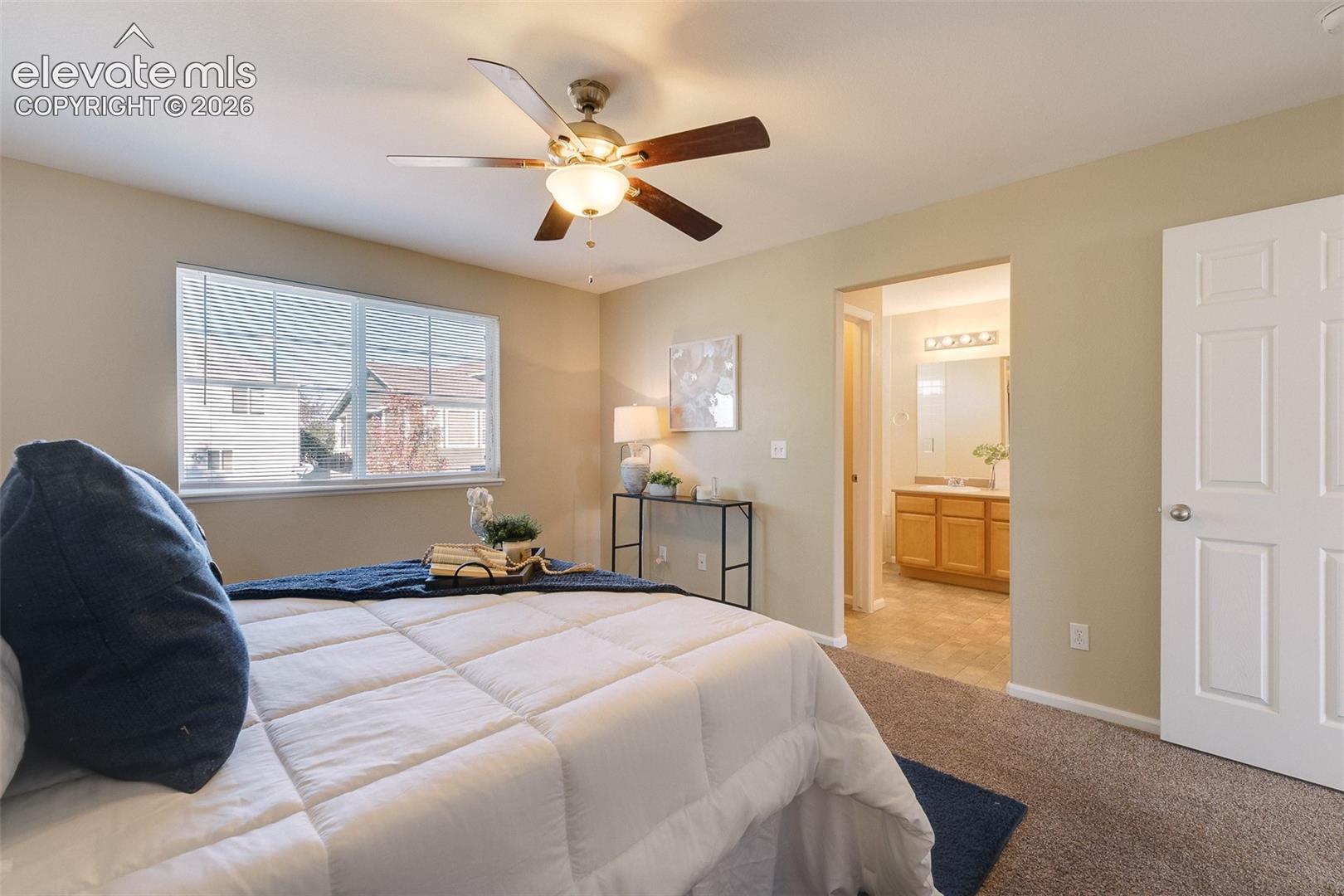 Neutral-toned interior featuring carpeted flooring, a ceiling fan with integrated lighting, a large window with horizontal blinds, and a multi-panel interior door