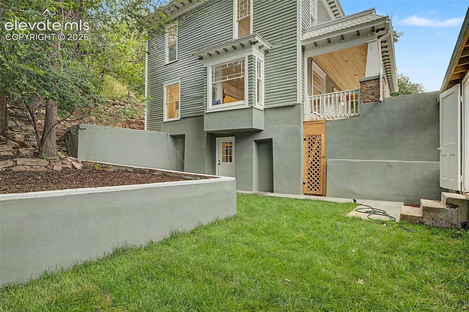 Expansive green lawn area featuring concrete retaining walls, an exterior entrance, and a wood lattice gate
