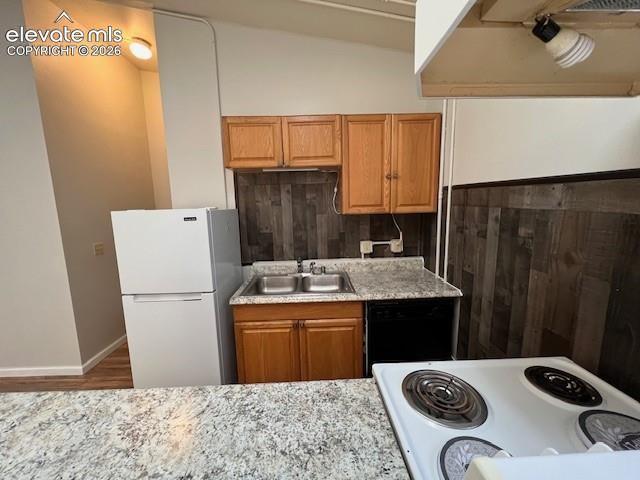 Kitchen featuring wood cabinetry, stone-finish countertops, a double-basin stainless steel sink, and wood-plank style wall accents