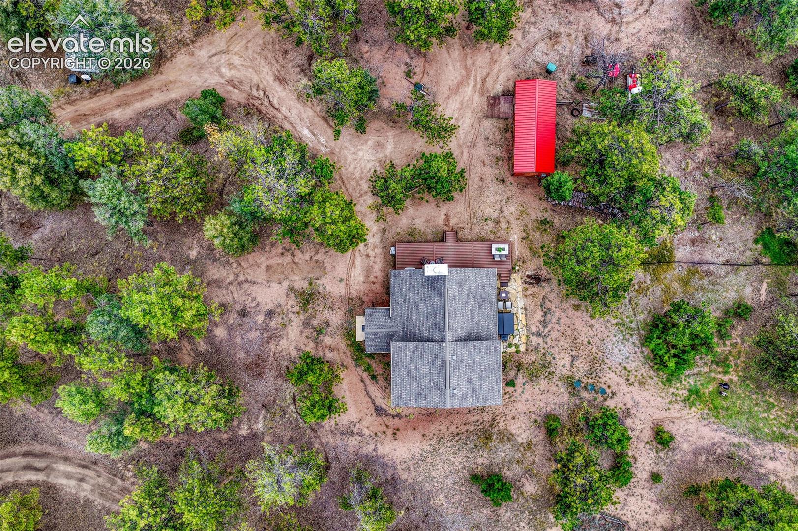 Aerial view of a sprawling wooded parcel featuring a primary structure with a shingled roof, a secondary red-roofed outbuilding, and an earthen driveway network