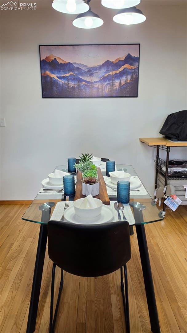 Dining area featuring wood-finish flooring, a glass-top table with black legs, and a black dining chair