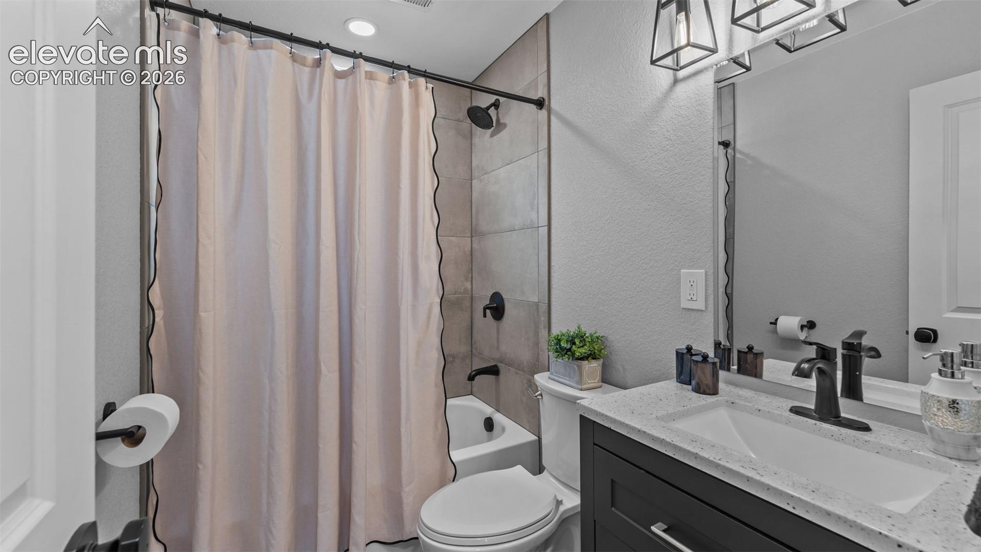 Bathroom featuring a dark wood-finish vanity with a light-toned solid surface countertop, an integrated rectangular sink, matte black hardware, and a tub-shower combination with floor-to-ceiling neutral tile surround