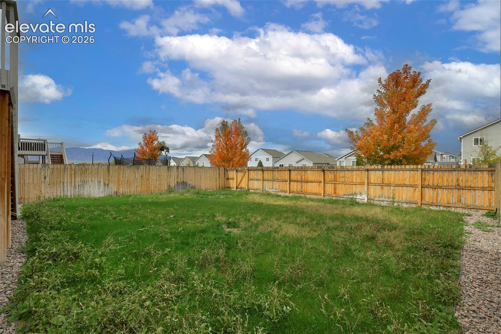 Rear yard featuring a wood privacy fence, gravel perimeter edging, and mature trees