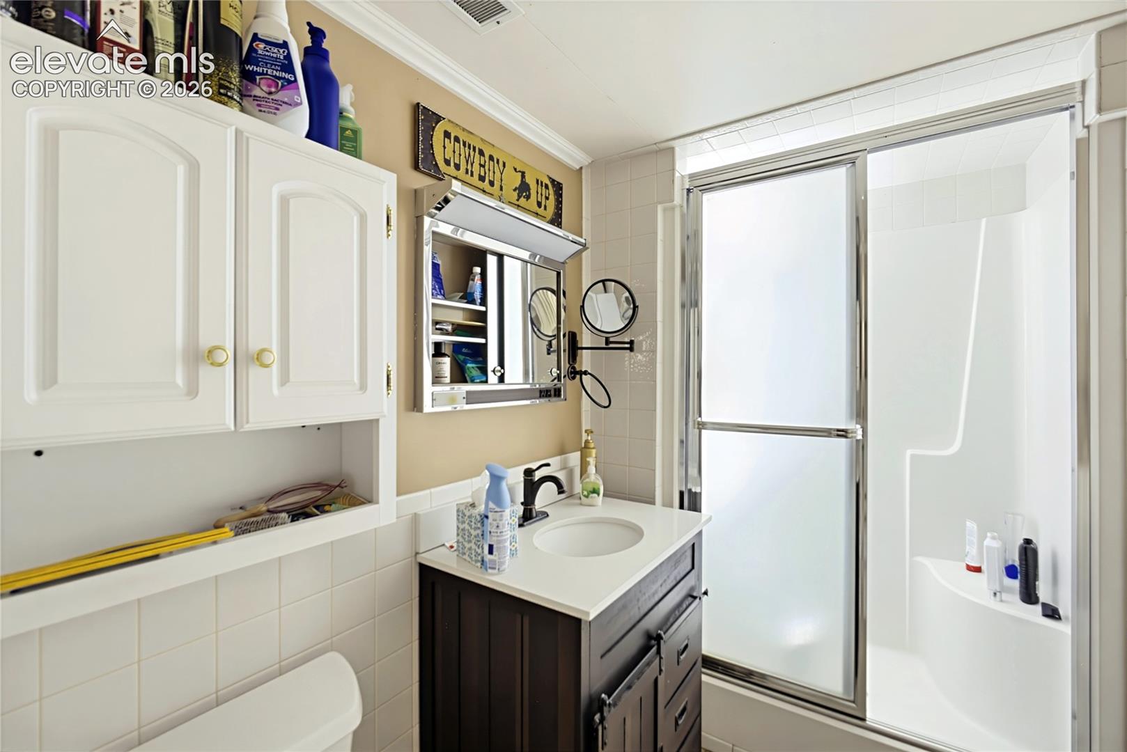 Bathroom featuring a dark wood-finish vanity with a white countertop, chrome hardware, a mirrored medicine cabinet, and a shower enclosure with a built-in seat and sliding glass doors