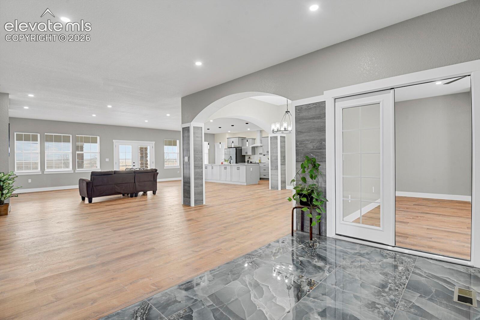 Open-concept interior featuring wood-finish flooring, a decorative arched entryway with vertical stone-finish paneling, recessed lighting, and large-format polished tile flooring in the entry