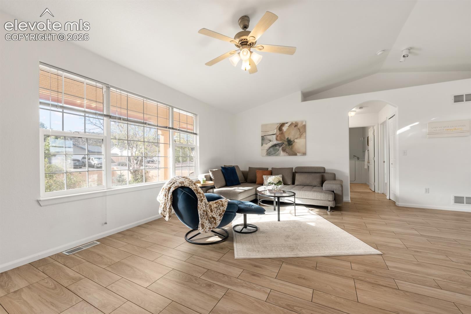 Vaulted ceilings, wood-finish tile flooring, large multi-pane windows, and a central ceiling fan with integrated lighting