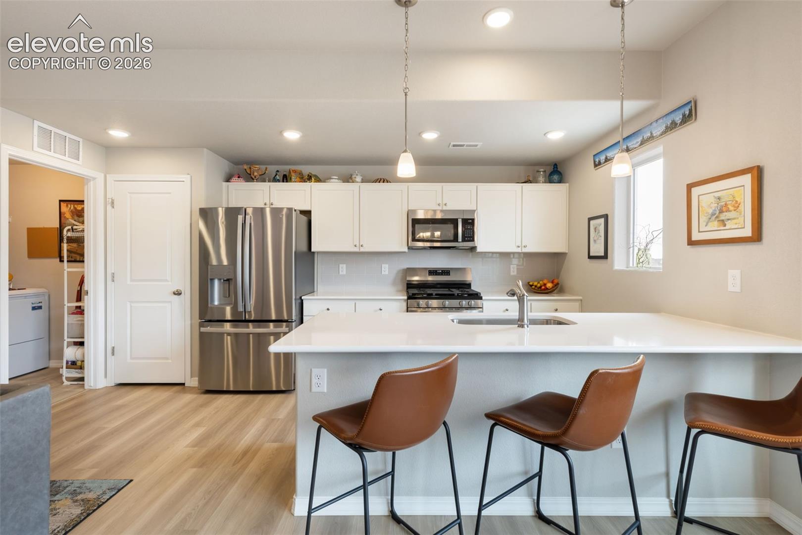 Modern kitchen featuring a large island with integrated sink, stainless steel appliances, white cabinetry, and wood-finish flooring