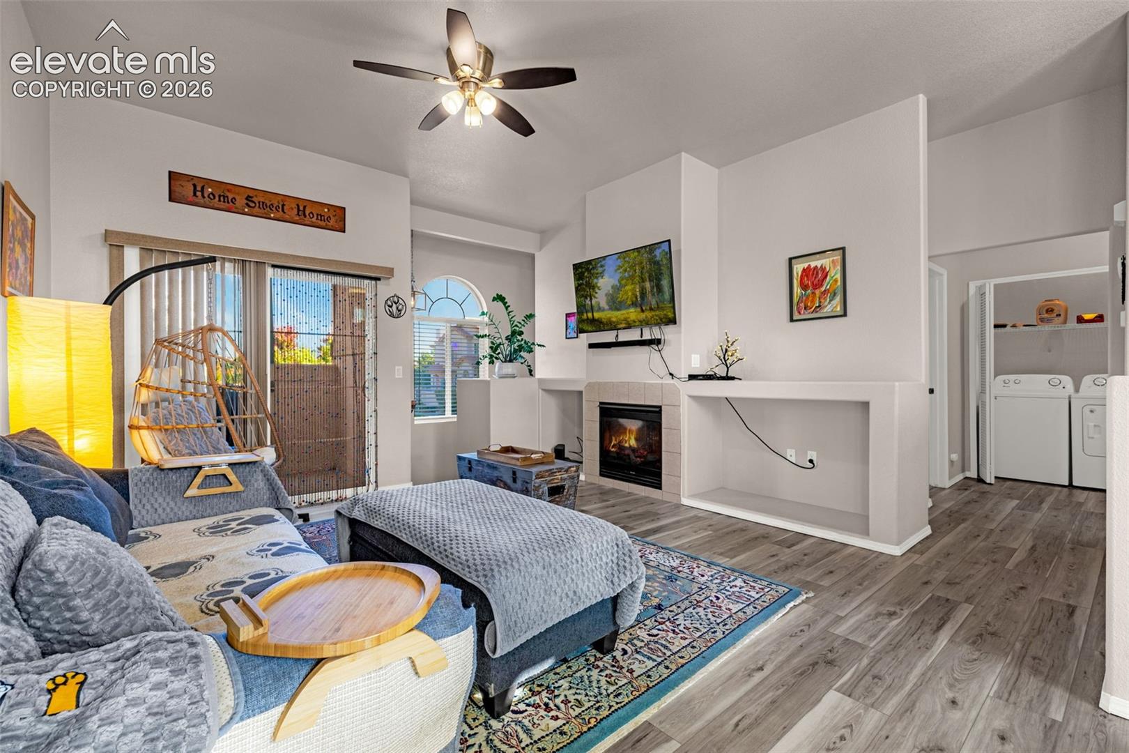 Living area featuring wood-finish flooring, a fireplace with tile surround, built-in shelving, an arched window, and sliding glass doors