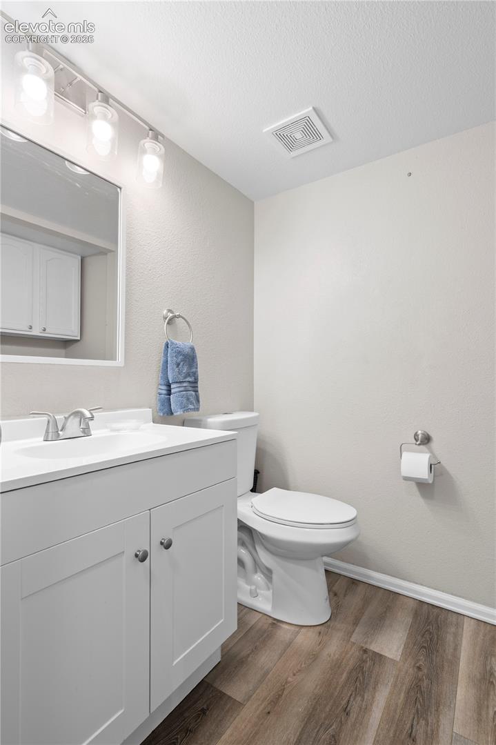 White vanity with integrated sink, polished chrome faucet, framed mirror, multi-bulb wall lighting, and wood-finish flooring