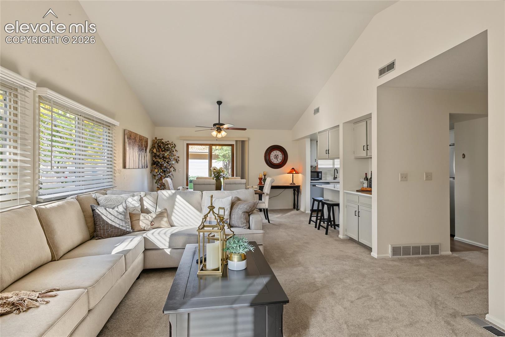Vaulted ceilings, large windows with blinds, ceiling fan, built-in cabinetry, and neutral-toned carpeting