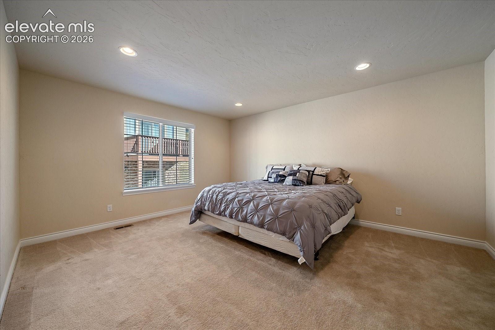 Neutral-toned bedroom featuring recessed lighting, carpeting, and a dual-pane window
