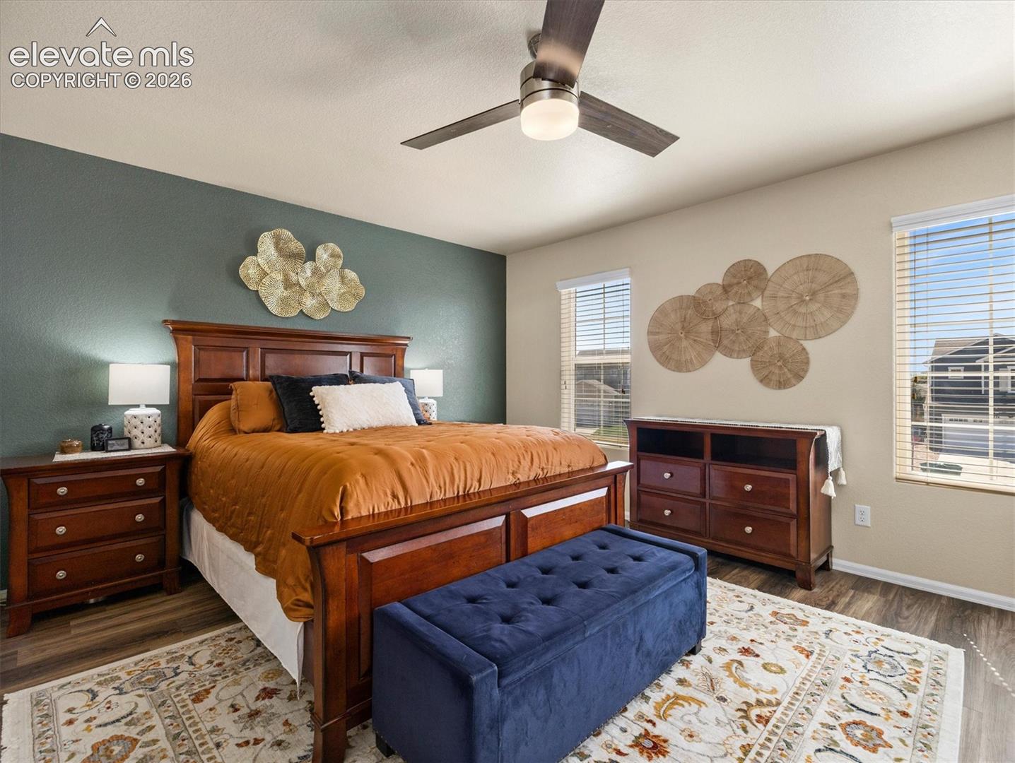 LVP flooring, two large windows with blinds, a ceiling fan with integrated lighting, and a neutral wall color complement a dark accent wall