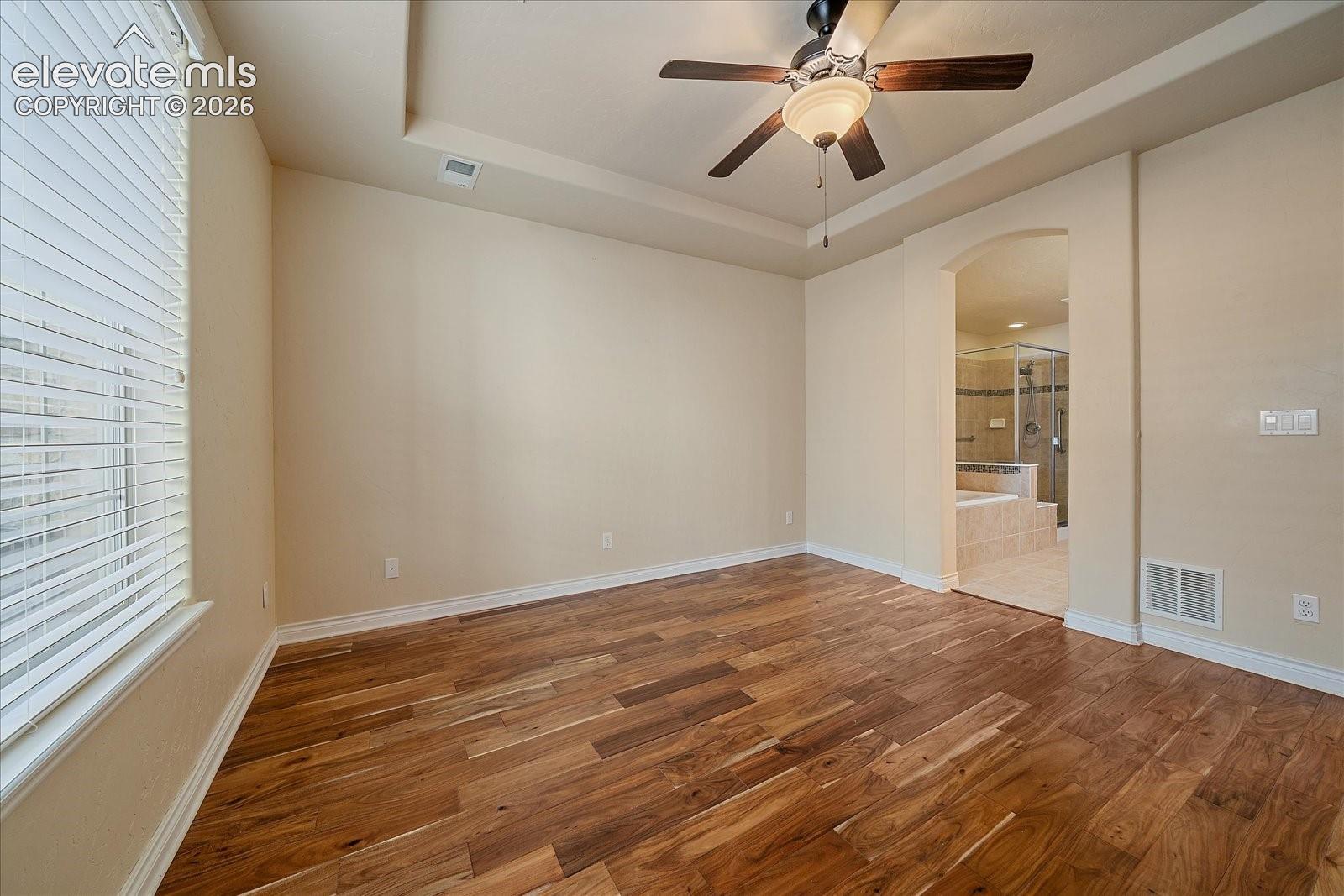 Room featuring wood-finish flooring, tray ceiling, ceiling fan with integrated lighting, and arched doorway