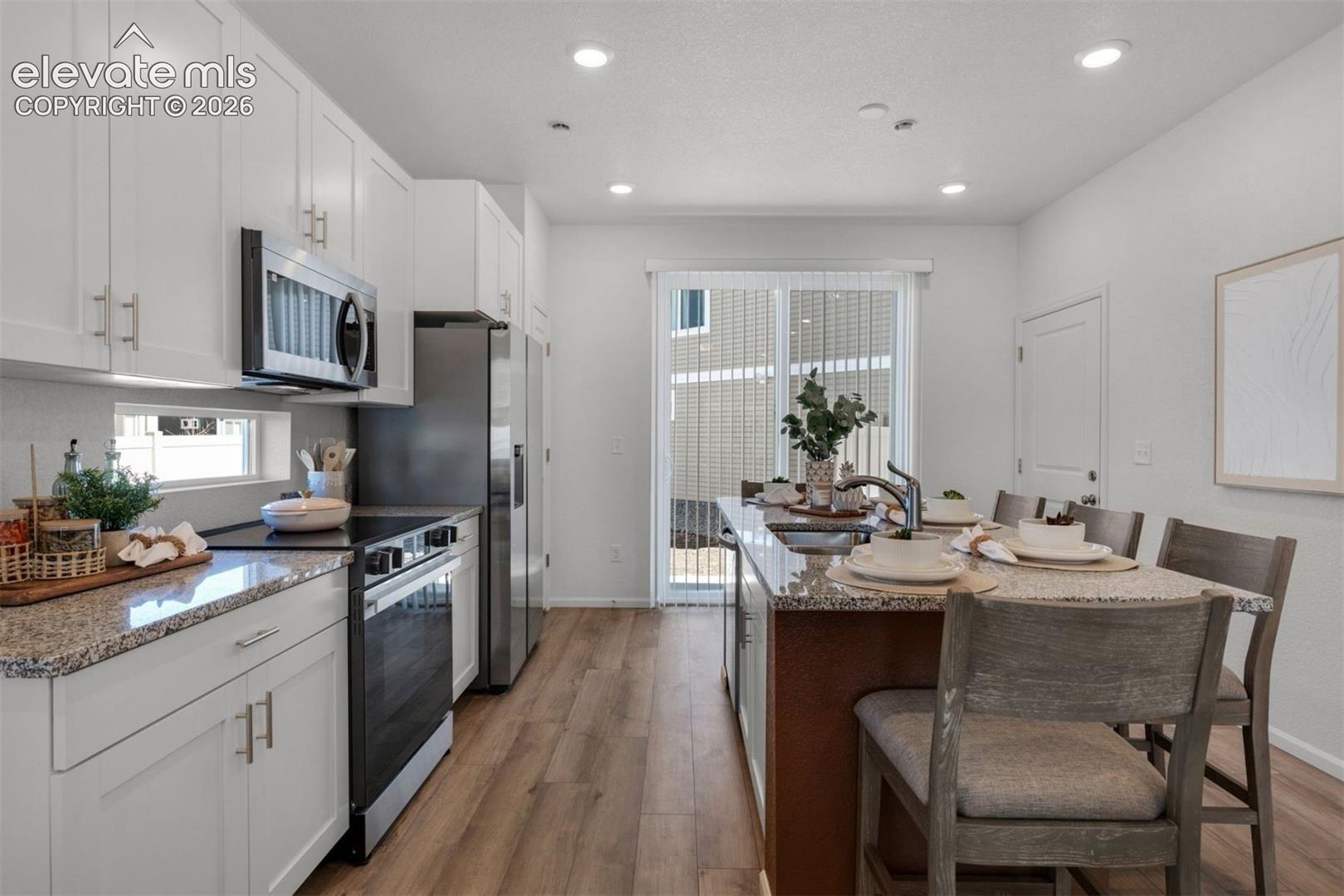 Kitchen featuring white cabinetry, stainless steel appliances, granite countertops, wood-finish flooring, and a sliding glass door
*photos of a model home*