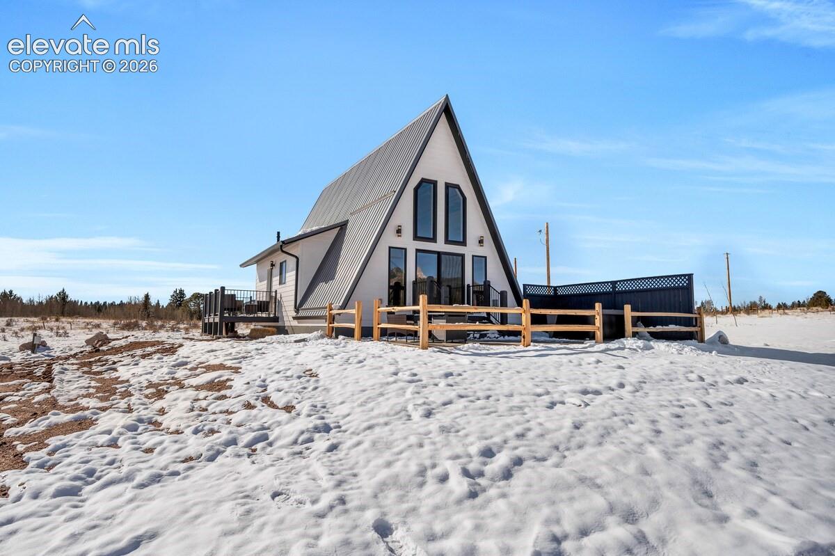 A-frame architecture featuring a metal roof, geometric windows, an elevated deck, and post-and-rail perimeter fencing