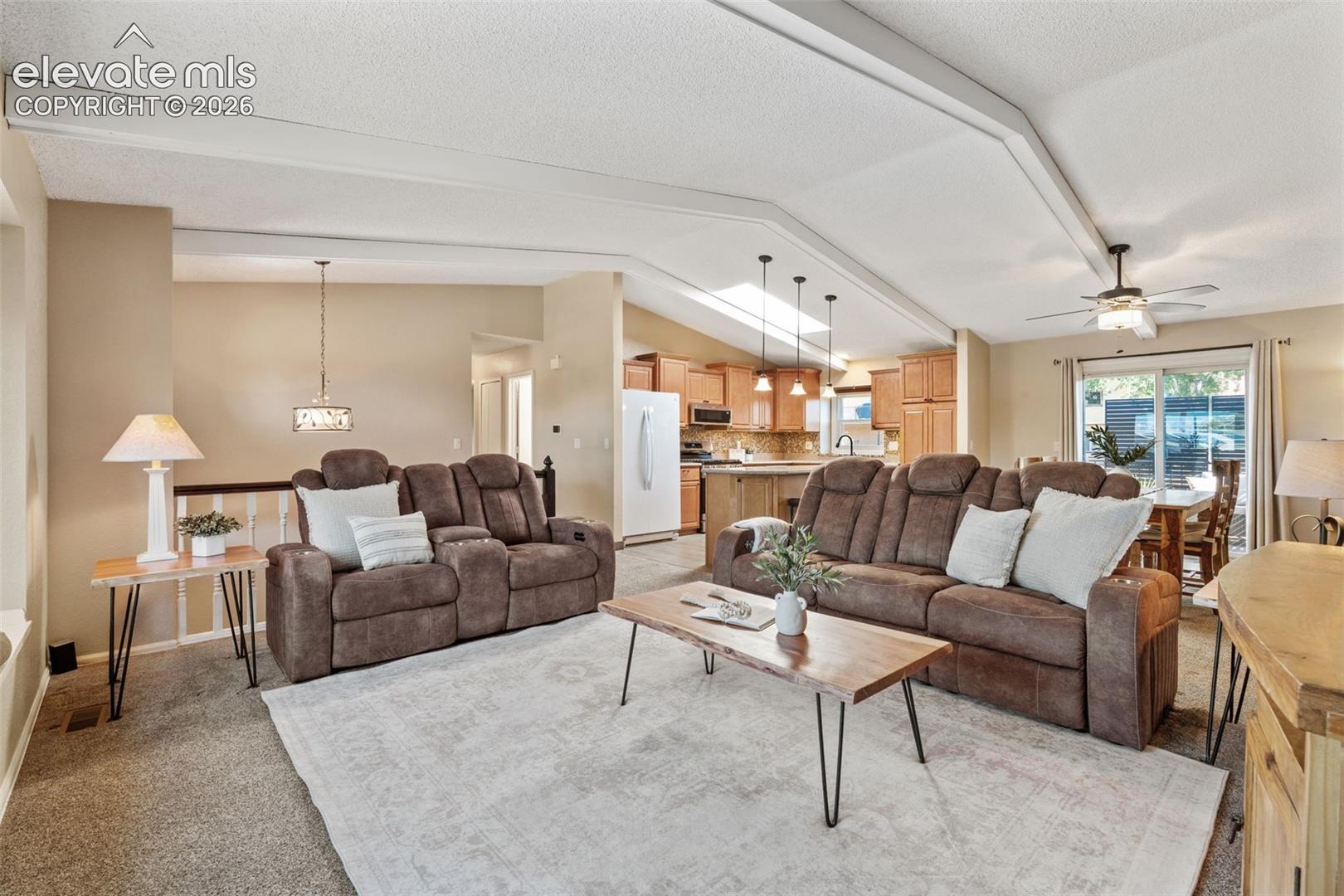 Open-concept interior featuring vaulted ceilings with exposed beams, a skylight, wood cabinetry, a center kitchen island, and a sliding glass door