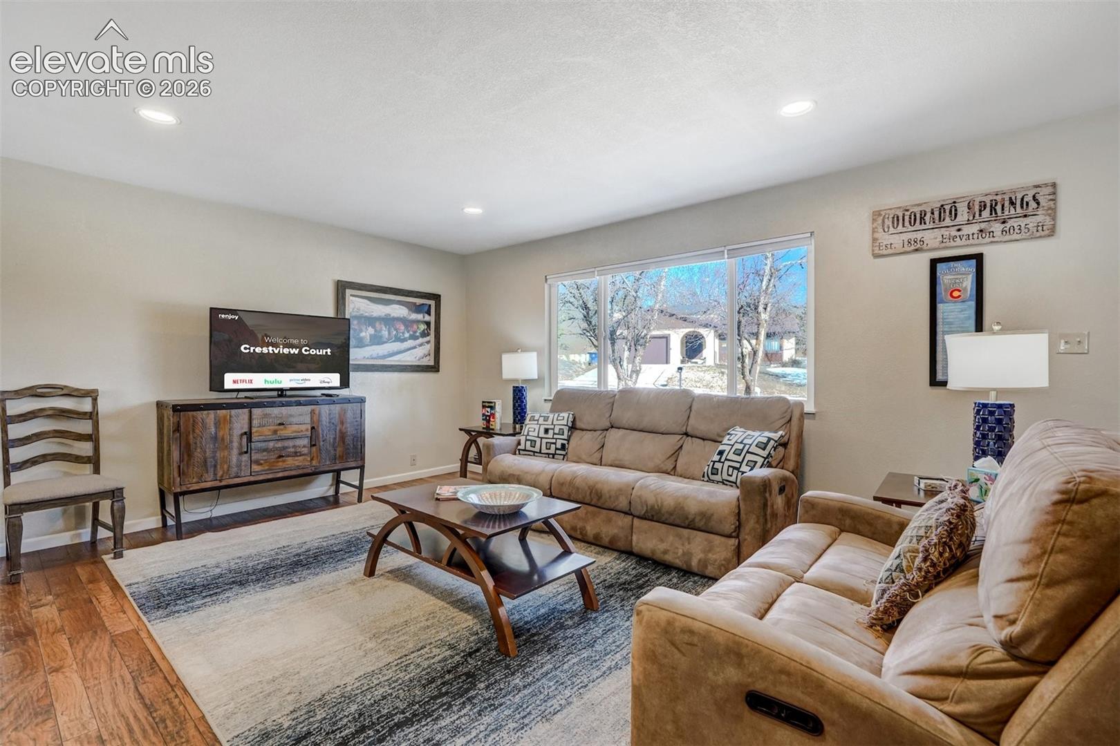 Recessed lighting, wood-finish flooring, a large window, and light-toned wall paint create a bright living space