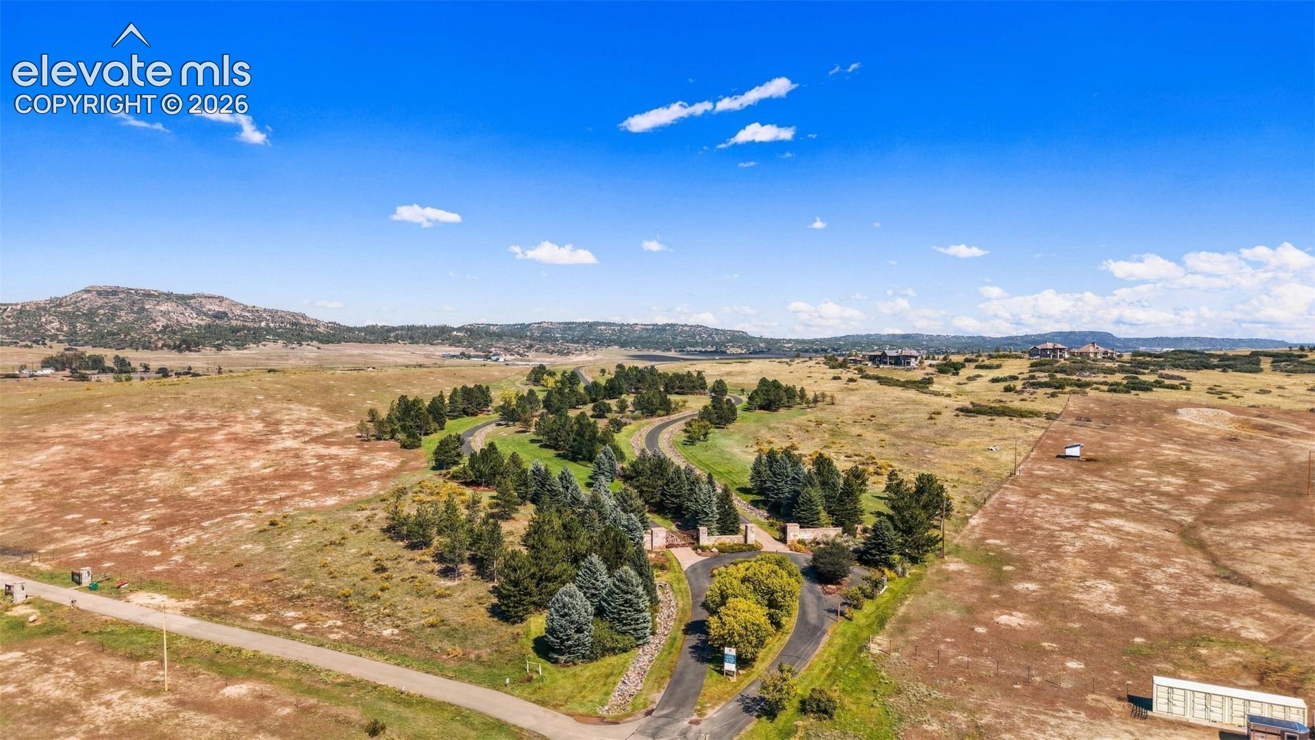 Expansive property with a paved access road, mature trees, and natural landscaping, set against a mountainous backdrop