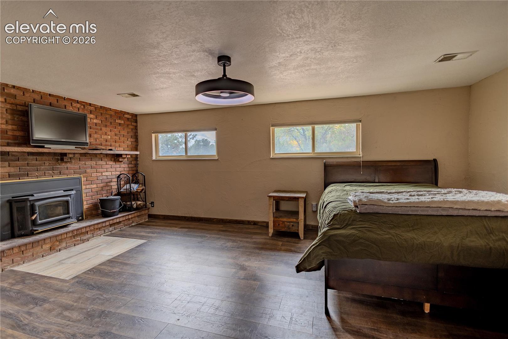 Exposed brick wall featuring an integrated fireplace with a wooden mantel, wood-finish flooring, and a modern circular ceiling fixture