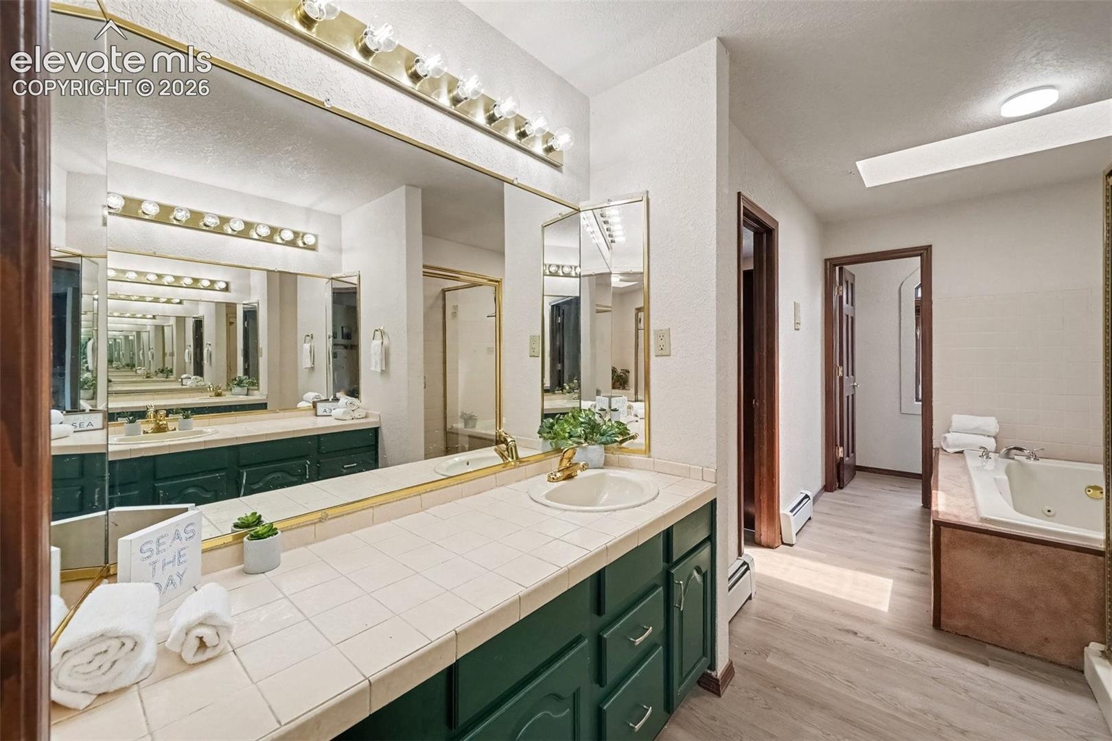 Beautiful primary bathroom featuring dual vanities, a spacious standing shower, skylight, and Jacuzzi tub