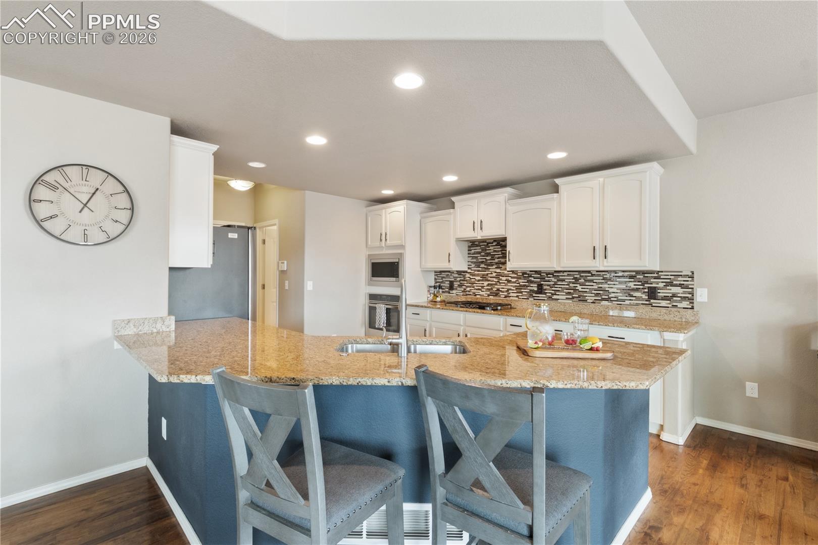 Kitchen featuring a peninsula, a kitchen breakfast bar, white cabinets, light stone counters, and dark wood-style flooring