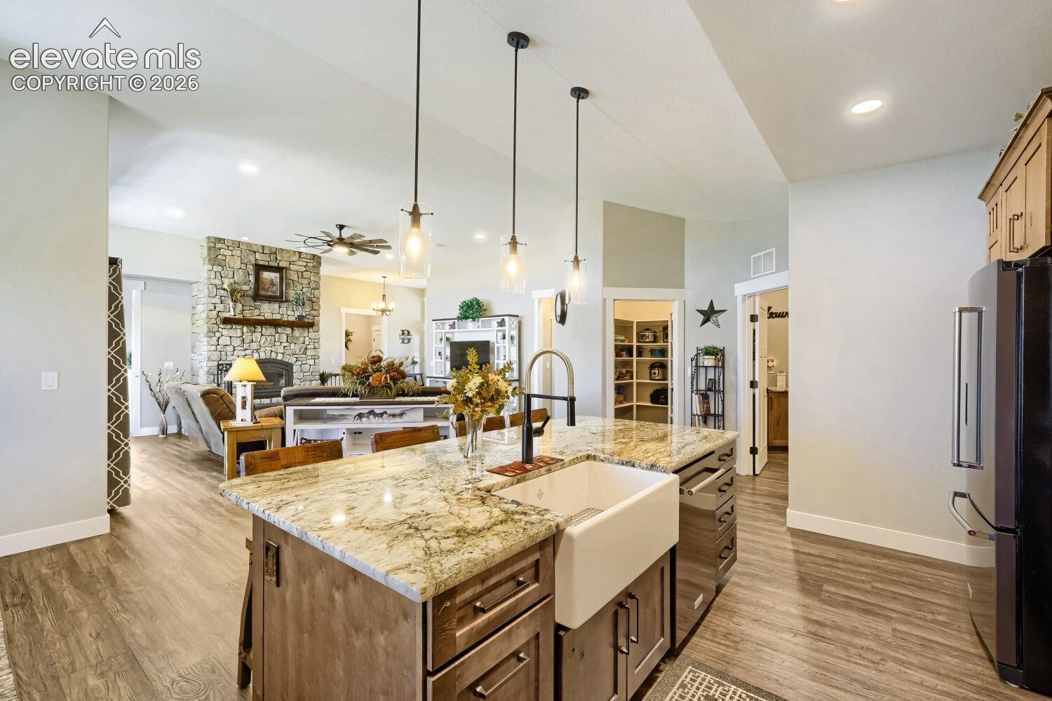 Kitchen island with a farmhouse sink, granite countertop, and pendant lighting