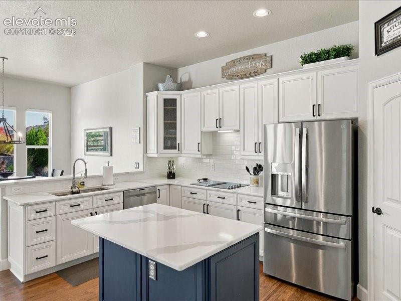 Chef's kitchen featuring white shaker cabinetry with black hardware, stainless steel French-door refrigerator, white quartz countertops, gas cooktop with range hood, and a navy blue center island with white countertop