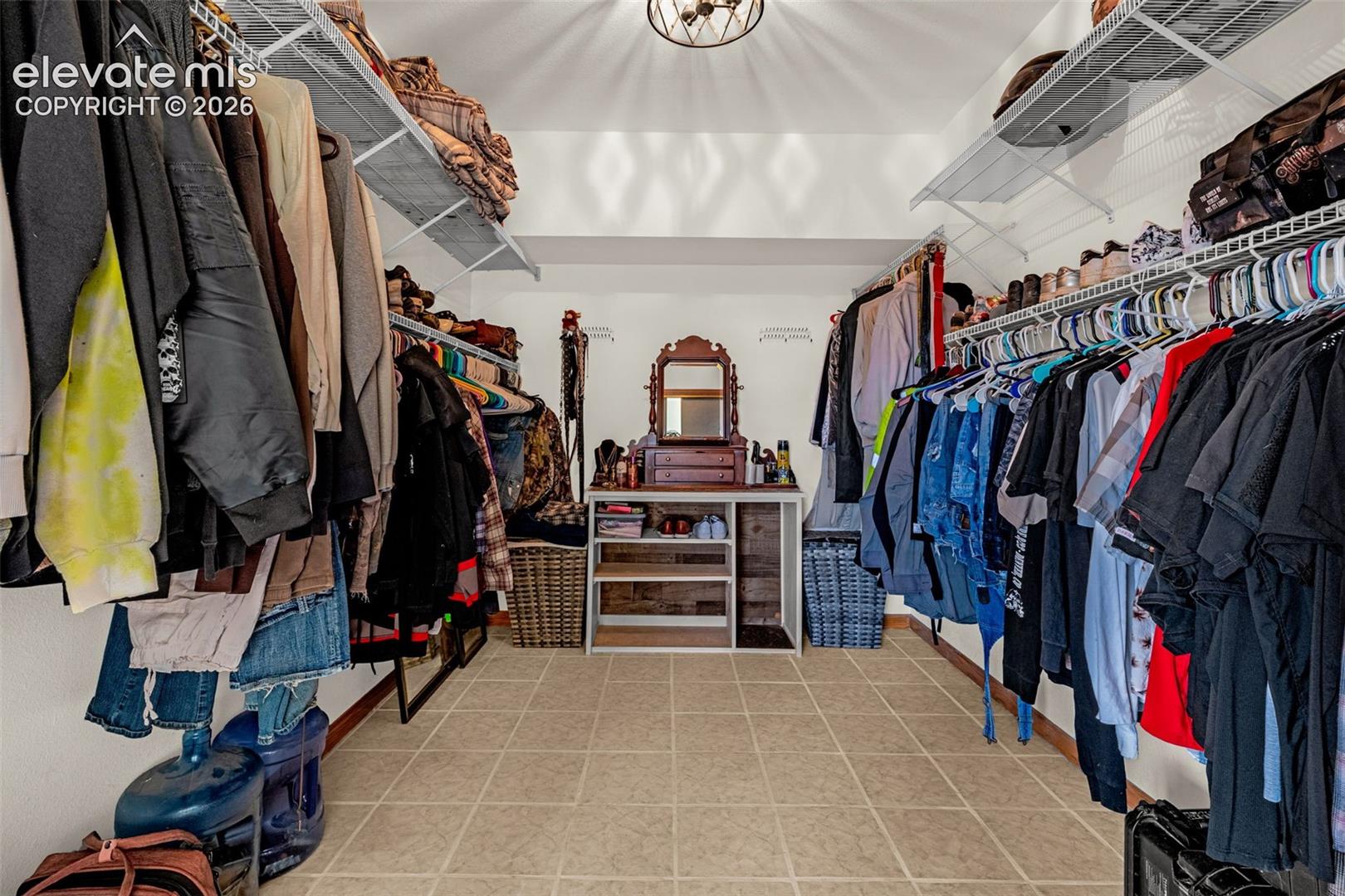 Walk-in closet featuring floor-to-ceiling adjustable wire shelving, ample hanging storage, and neutral-toned floor tiling