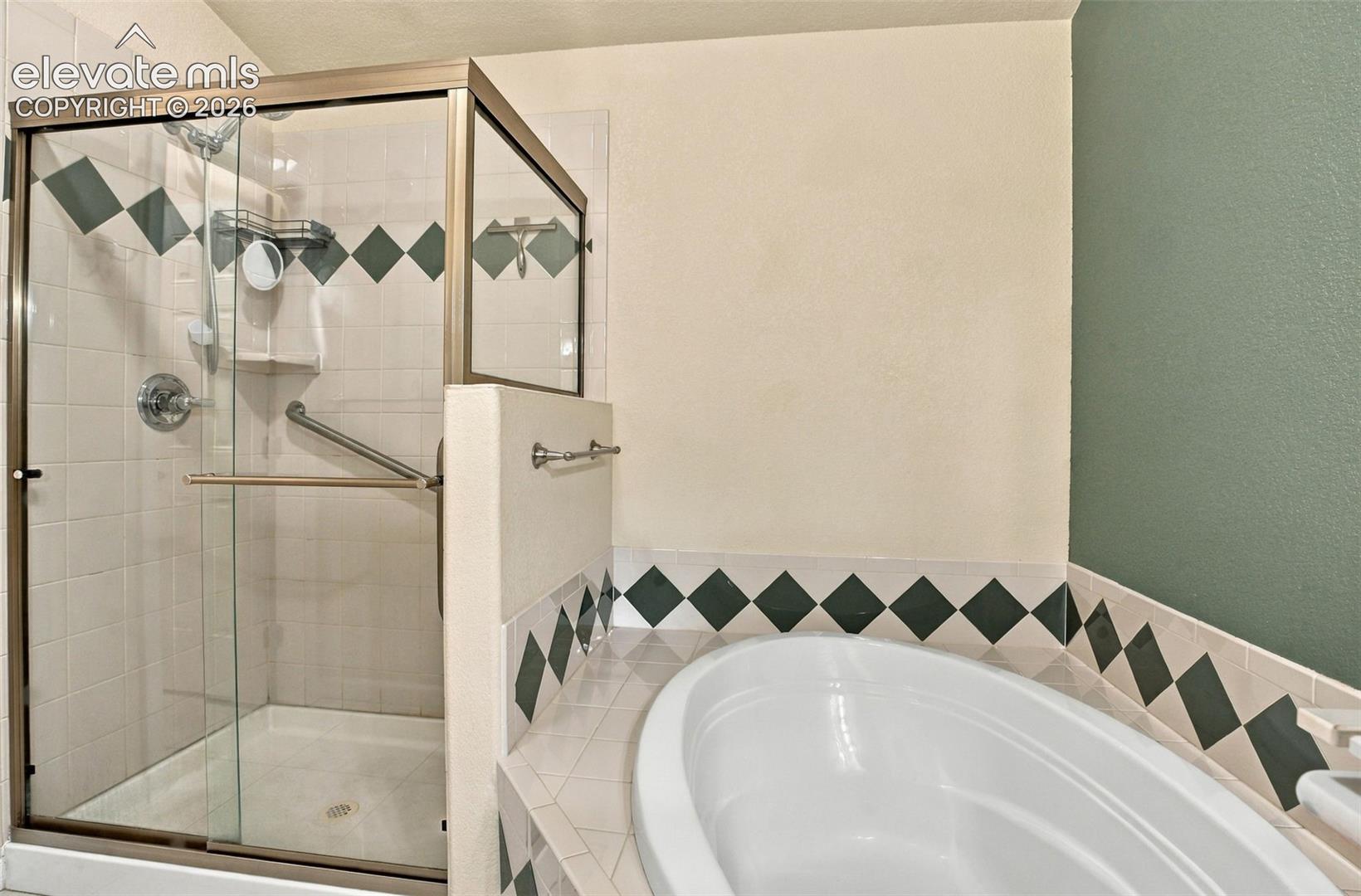 Bathroom featuring a glass-enclosed shower with metallic framing, built-in grab bars, and an oval soaking tub, finished with decorative diamond-patterned wall tiling