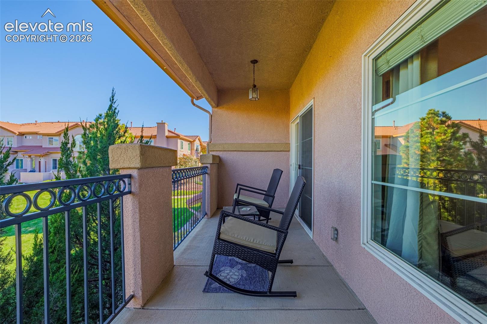 Covered balcony featuring stucco-finished walls, a decorative metal railing, concrete flooring, and an integrated hanging light fixture