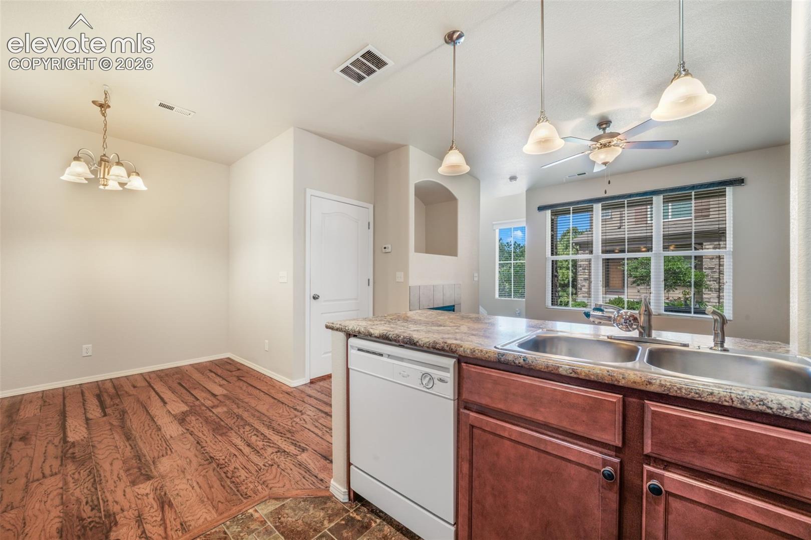 Open-concept kitchen and dining area featuring warm wood-finish flooring, granite countertops, cherry cabinetry with stainless steel appliances, pendant lighting, and expansive windows with natural light