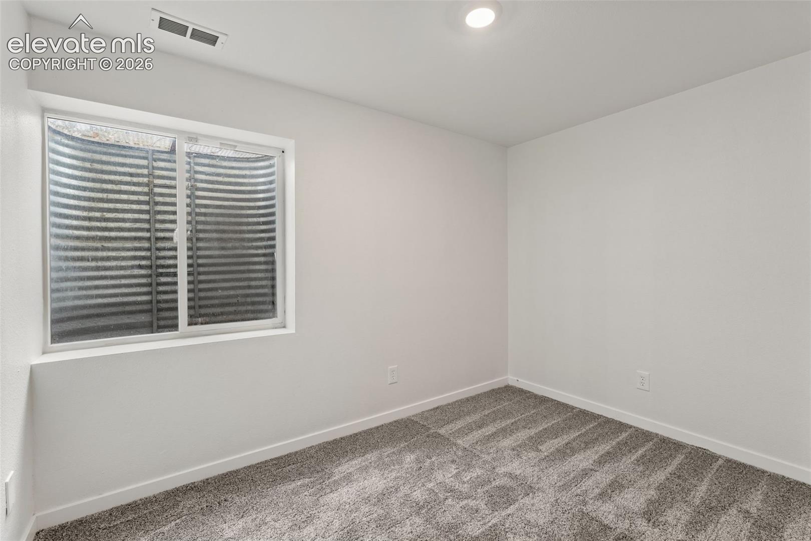 Neutral-toned wall-to-wall carpeting, recessed ceiling lighting, and a sliding window with a corrugated metal egress well
