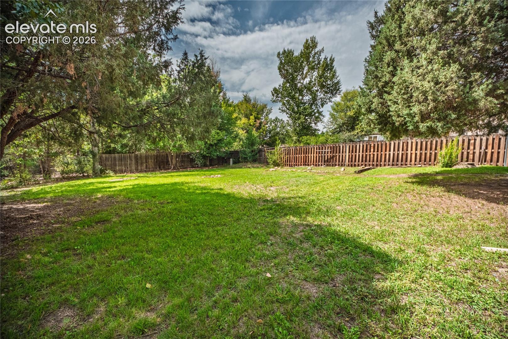 Expansive grassy yard with mature trees and a wood privacy fence