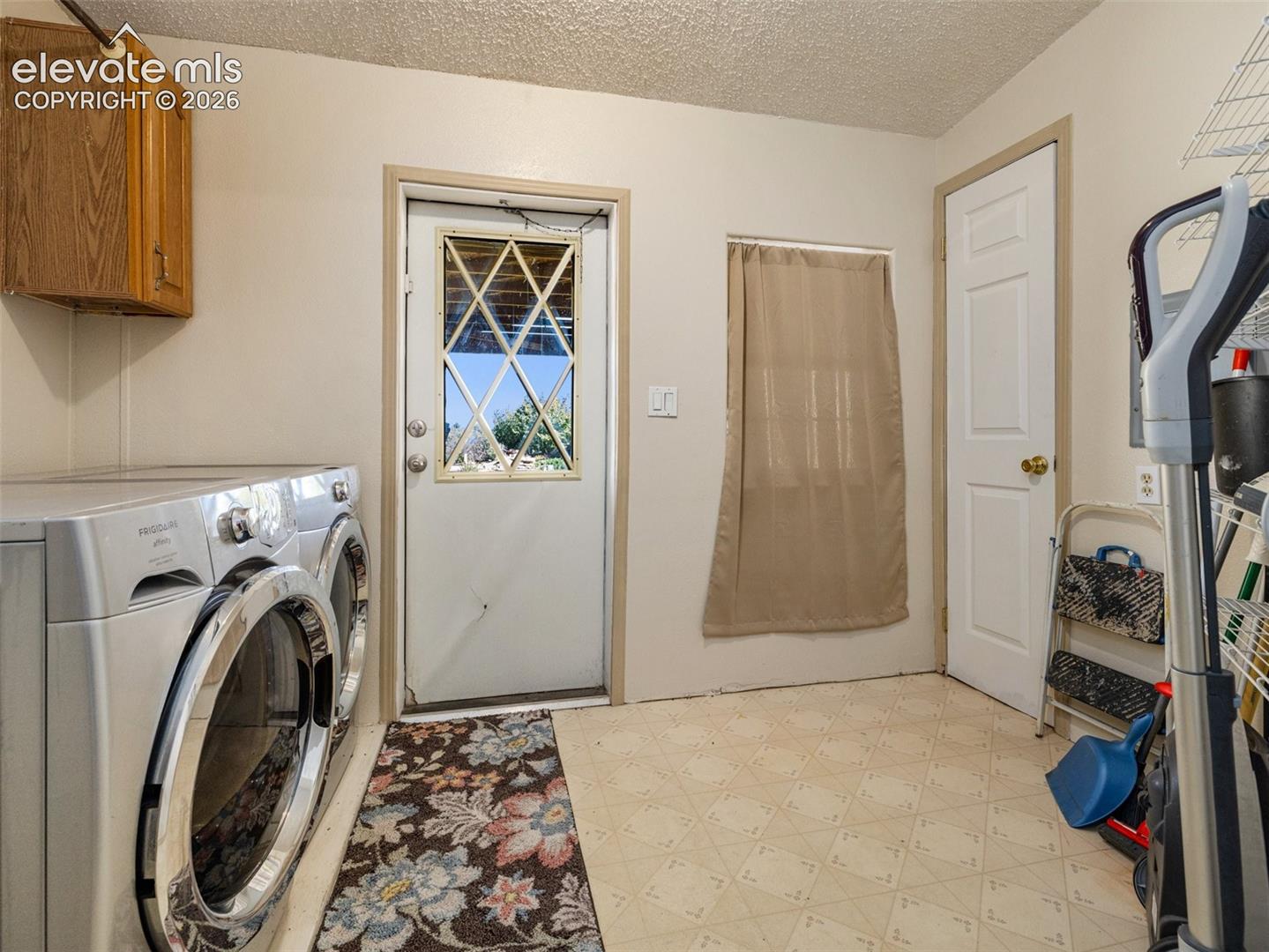 Utility area featuring wall-mounted wooden cabinetry, a metal exterior door with a diamond-patterned window insert, and resilient sheet flooring