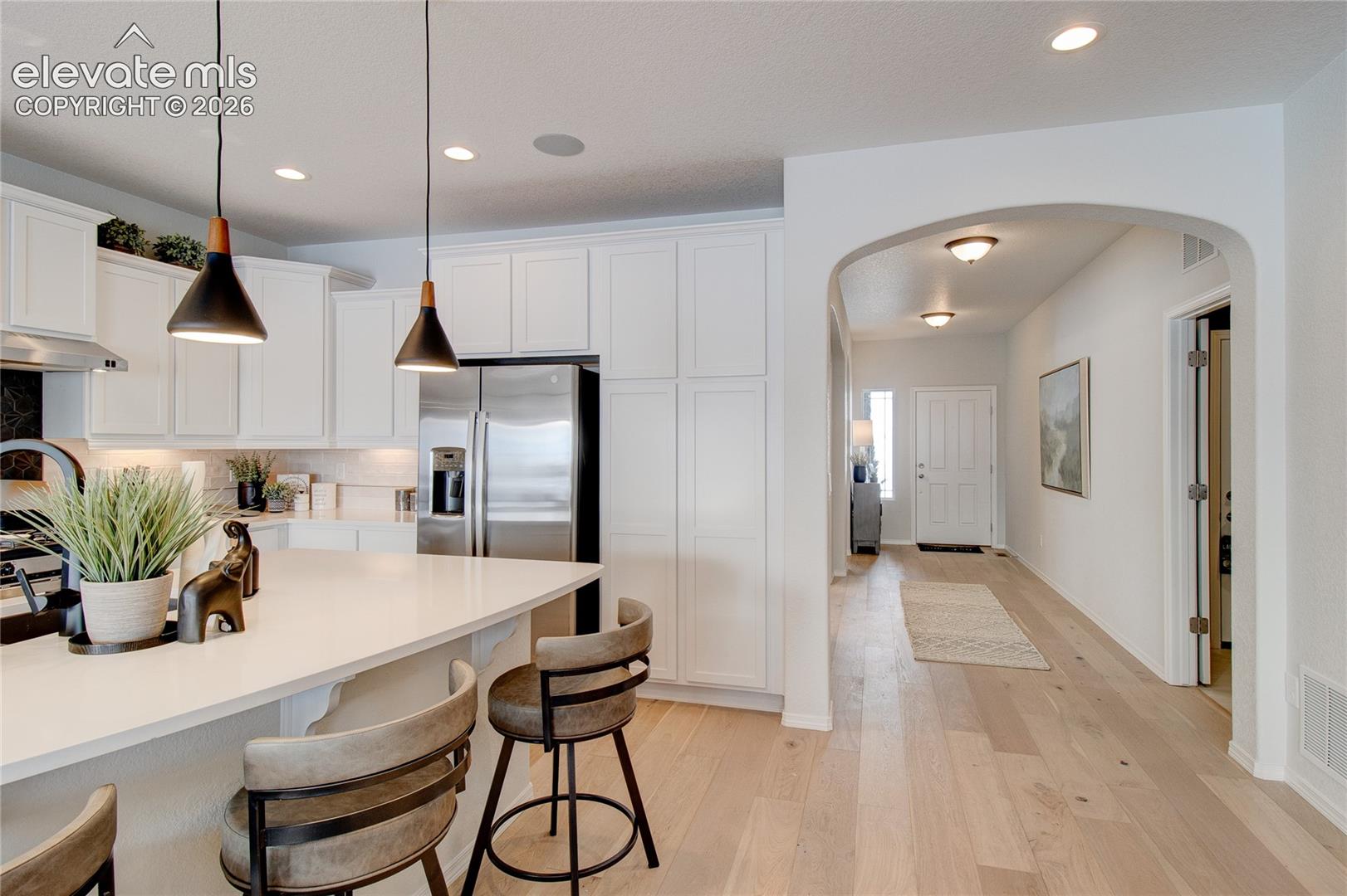 Kitchen featuring white cabinetry, an expansive island with solid-surface countertop, recessed lighting, and modern pendant fixtures, accented by wood-finish flooring and an arched entryway