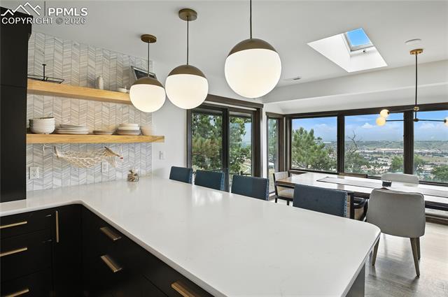 Kitchen with hanging light fixtures, dark cabinets, tasteful backsplash, a skylight, and open shelves