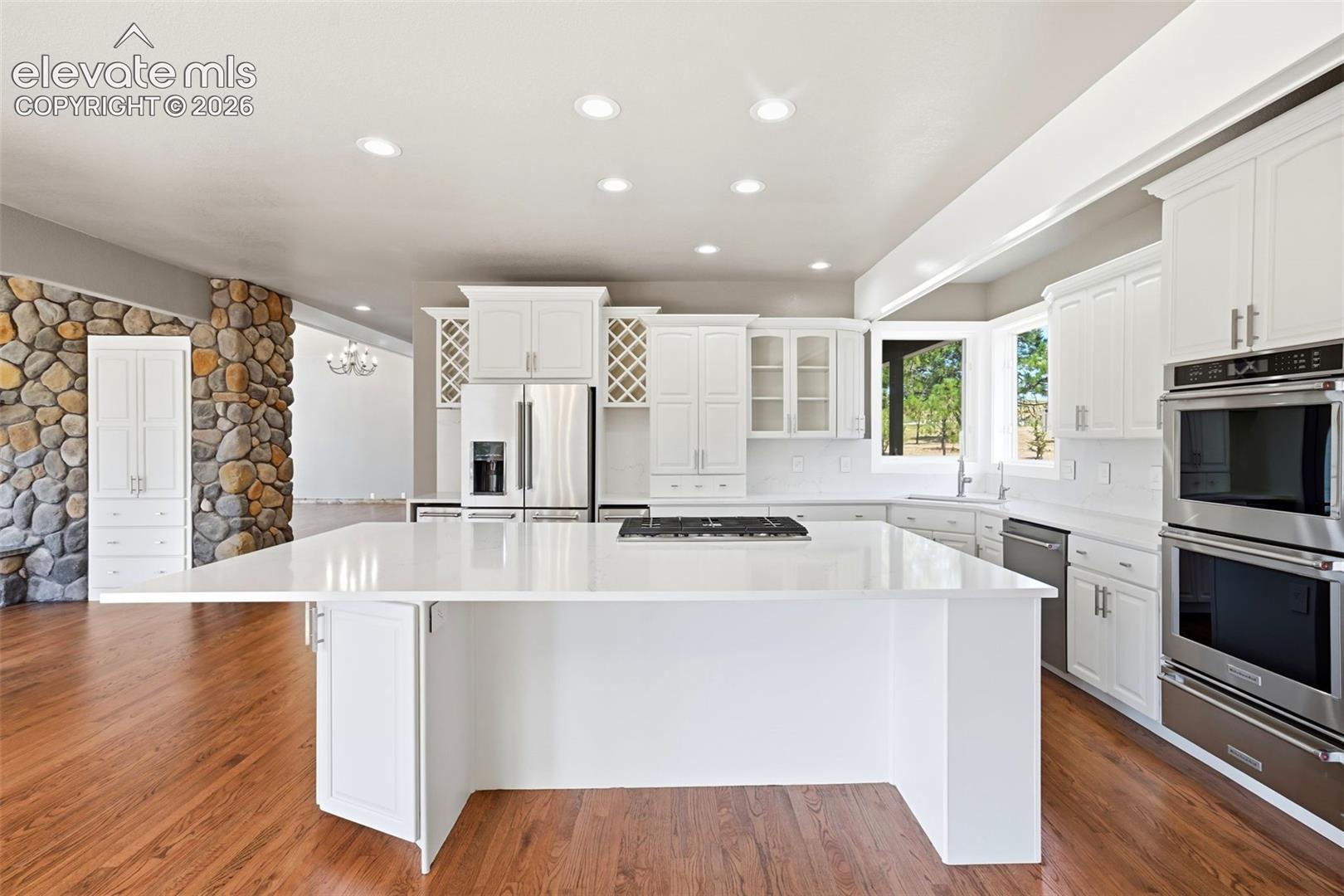 Contemporary kitchen featuring a large central island with a cooktop, white cabinetry, integrated stainless steel appliances, and wood-finish flooring