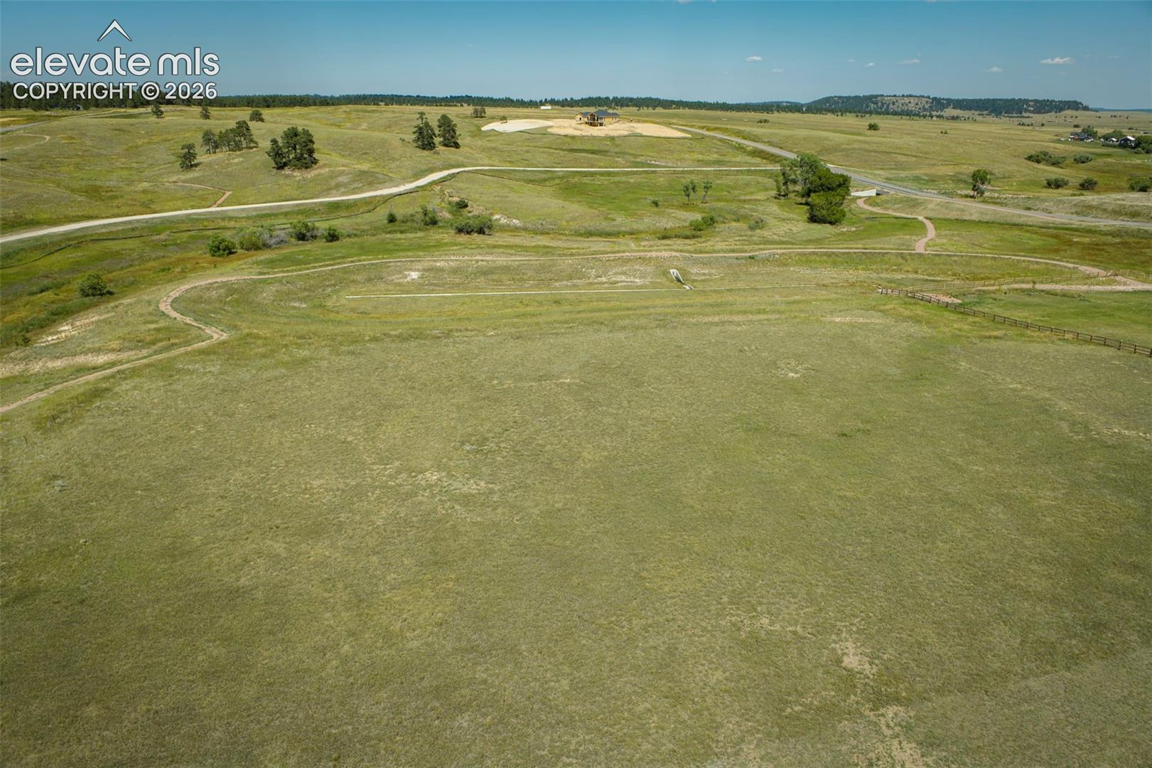 Expansive acreage featuring rolling topography, open grassy meadows, scattered clusters of mature trees, and existing dirt access roads