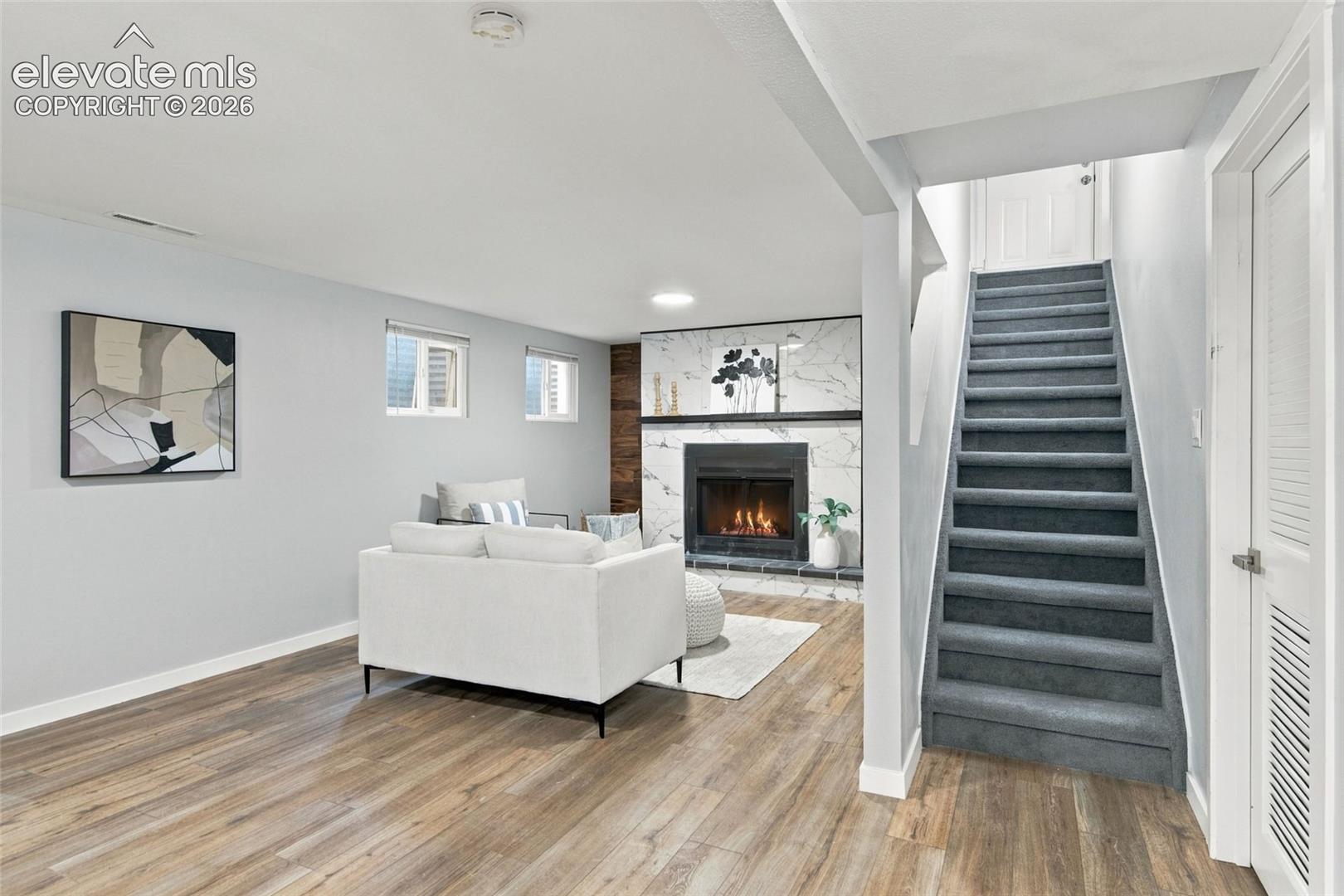 Finished interior space featuring wood-finish flooring, a stone-surround fireplace, and carpeted staircase