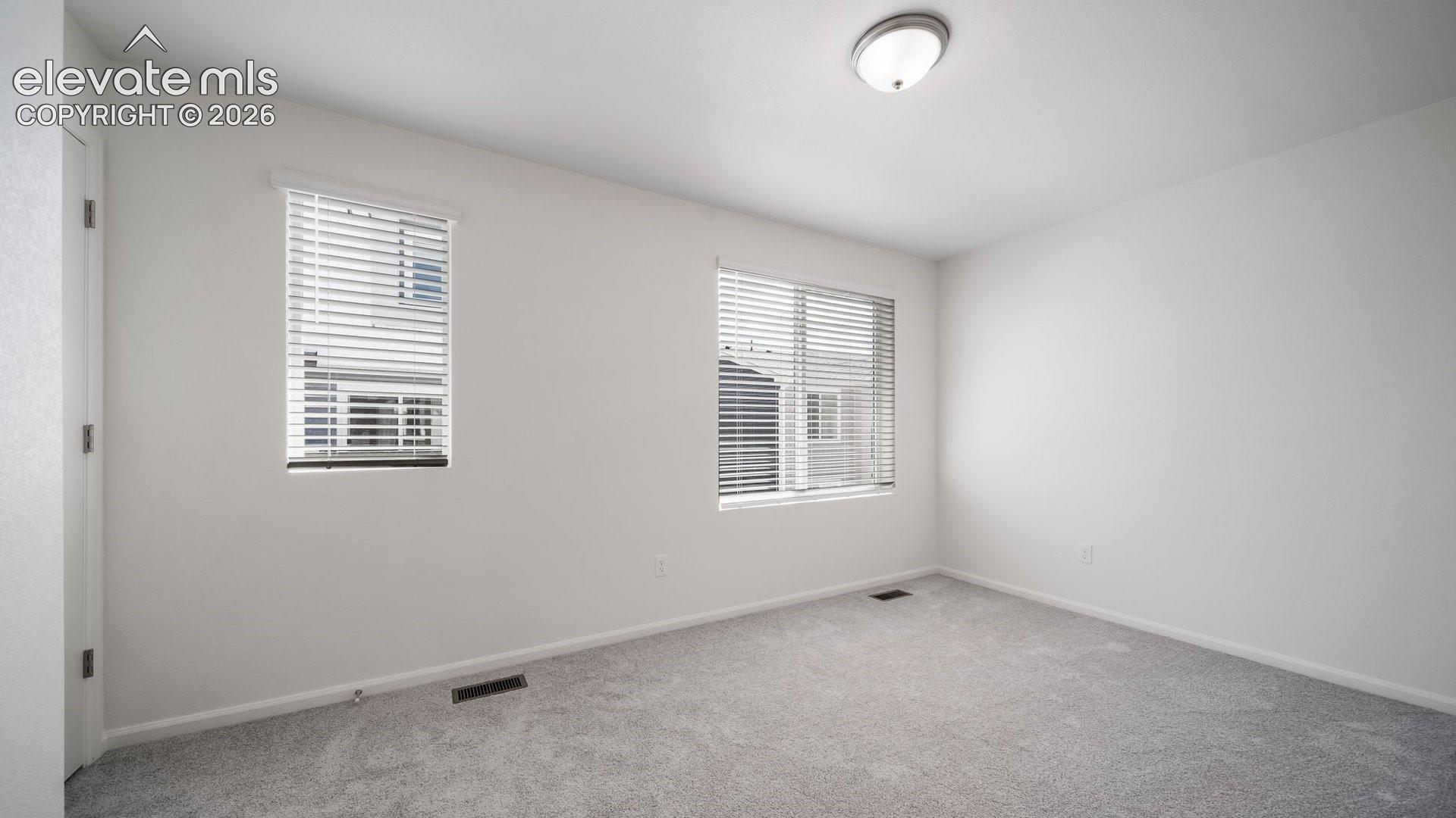 Neutral-toned carpet flooring, two windows with horizontal blinds, and a central ceiling-mounted light fixture
*photos of a model home*