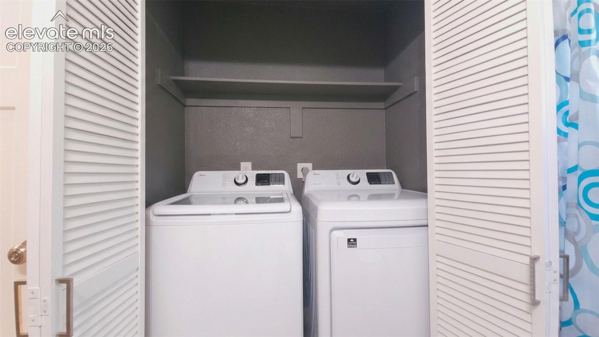 Laundry closet with louvered bi-fold doors, built-in shelving, and white washer and dryer units