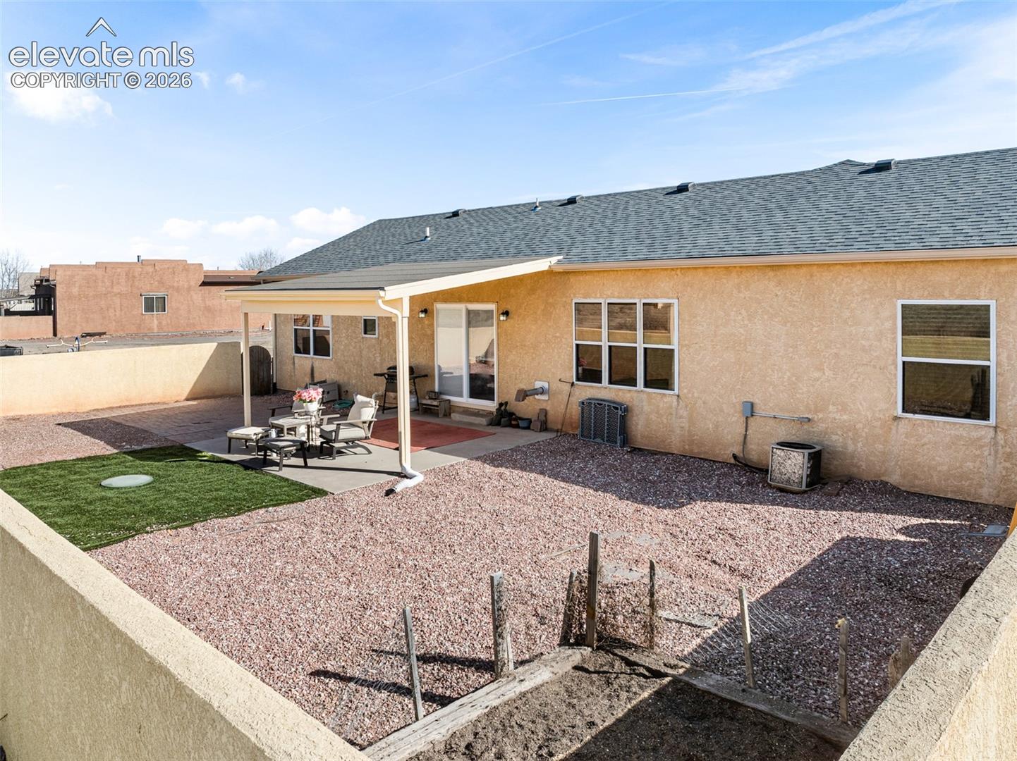 Expansive backyard featuring a covered patio, xeriscape landscaping, a small grassy area, and perimeter fencing