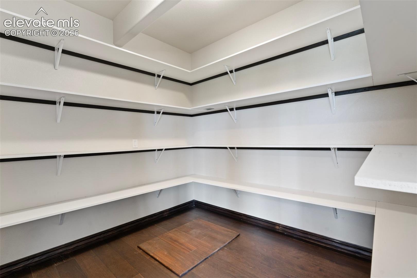 Spacious pantry featuring extensive white shelving, and dark wood-finish flooring
