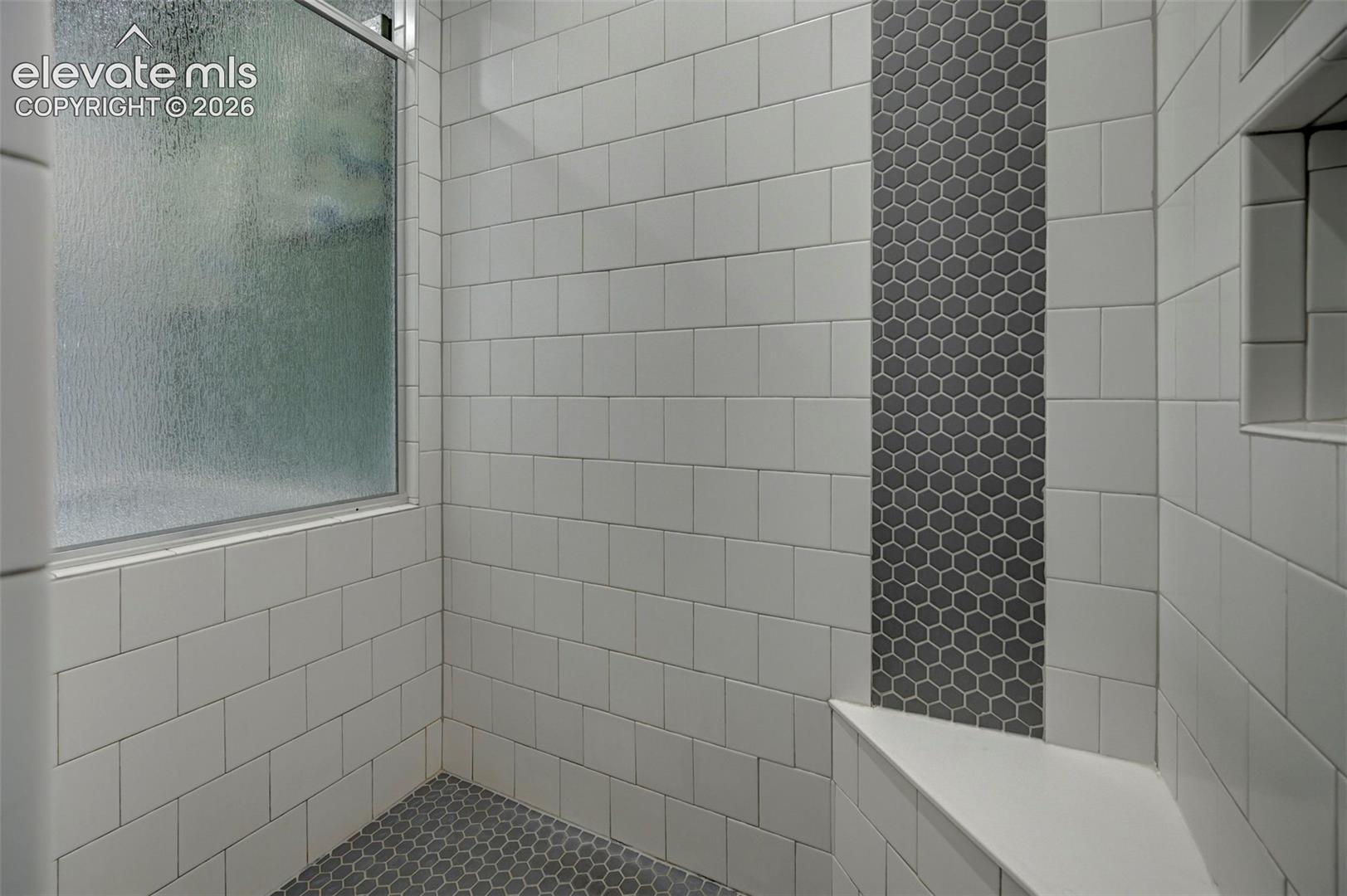 Shower enclosure featuring white subway tile, a frosted window, a dark hexagon mosaic tile accent strip, a built-in shower niche, and an integrated shower bench