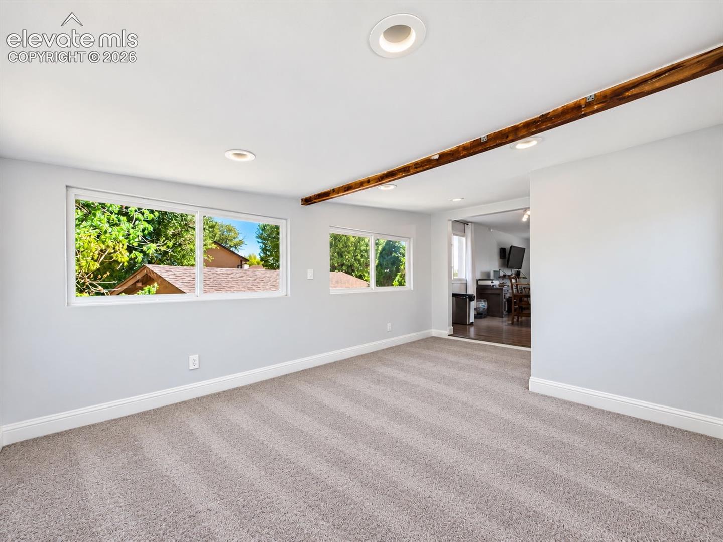 Additional sunroom view highlights the expansive carpeted floor area, multiple windows, recessed lighting, exposed wood beam, and easy connection to the kitchen.