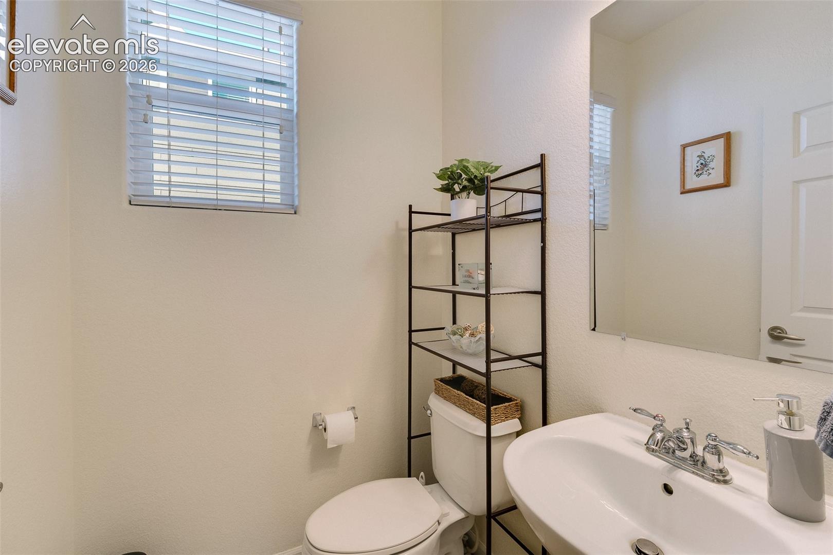 Recessed window with blinds, wall-mounted mirror, white pedestal sink with chrome faucet, and a two-panel interior door